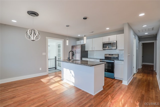 kitchen with stainless steel appliances, an island with sink, pendant lighting, light hardwood / wood-style floors, and white cabinets