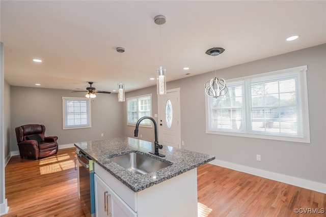 kitchen with white cabinets, sink, dark stone countertops, light wood-type flooring, and decorative light fixtures