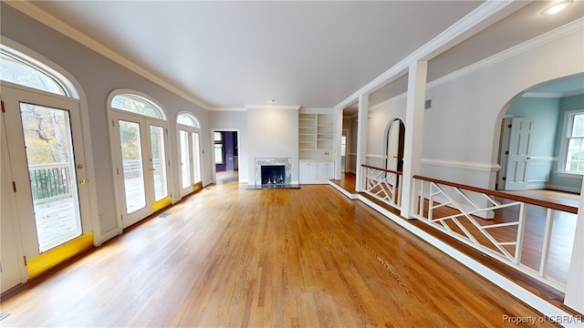 unfurnished living room with crown molding, built in features, and light wood-type flooring