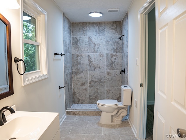 bathroom featuring a textured ceiling, vanity, tiled shower, tile patterned flooring, and toilet