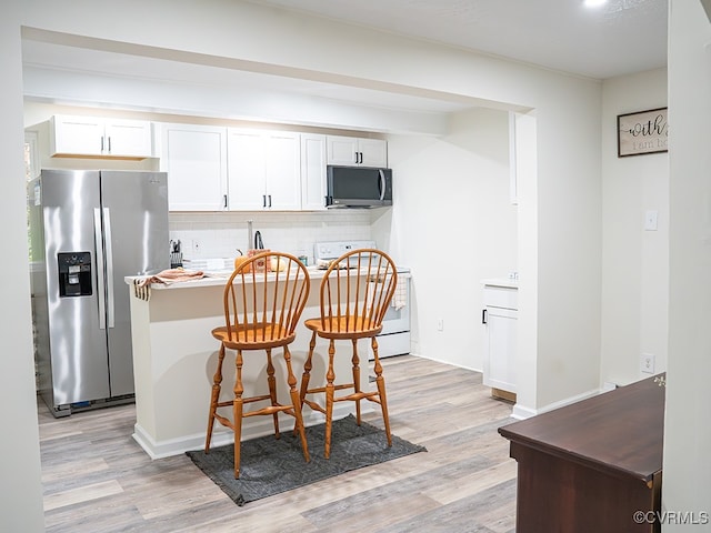 kitchen with a kitchen breakfast bar, white cabinetry, appliances with stainless steel finishes, and light hardwood / wood-style flooring