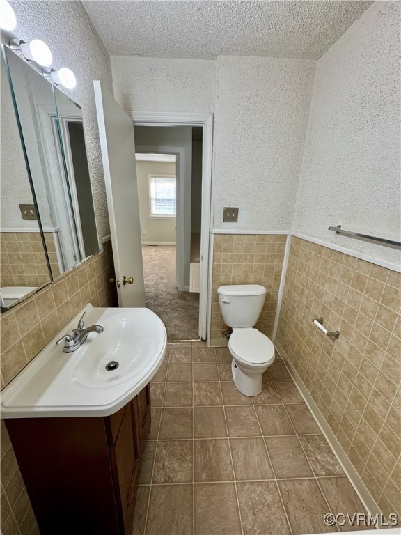 bathroom featuring tile patterned floors, vanity, a textured ceiling, tile walls, and toilet