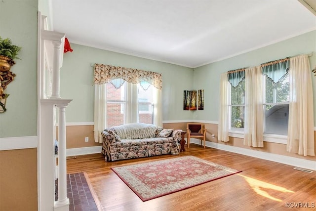 living area featuring hardwood / wood-style flooring, ornate columns, crown molding, and a wealth of natural light