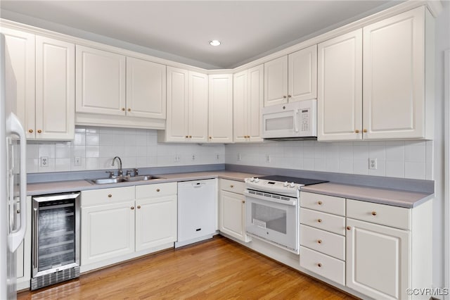 kitchen with wine cooler, white appliances, white cabinetry, and a sink