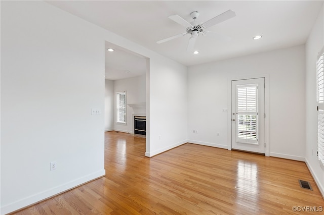 spare room with light wood-type flooring, visible vents, a fireplace with flush hearth, baseboards, and ceiling fan