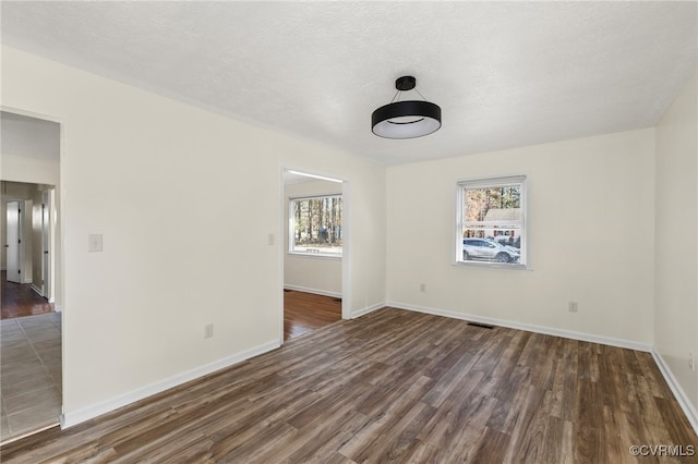 spare room featuring a healthy amount of sunlight, dark hardwood / wood-style flooring, and a textured ceiling