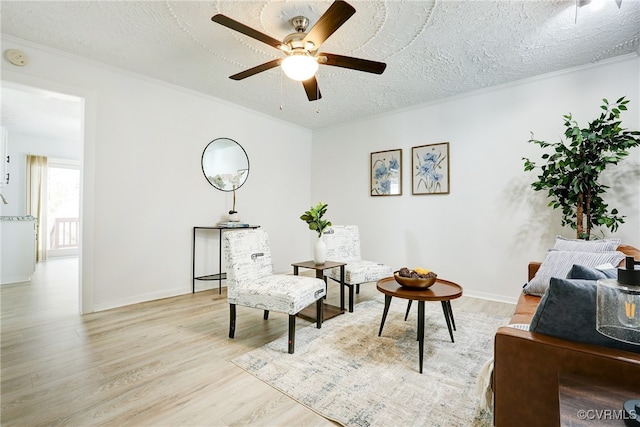 living area featuring light wood-type flooring, a textured ceiling, ceiling fan, and ornamental molding