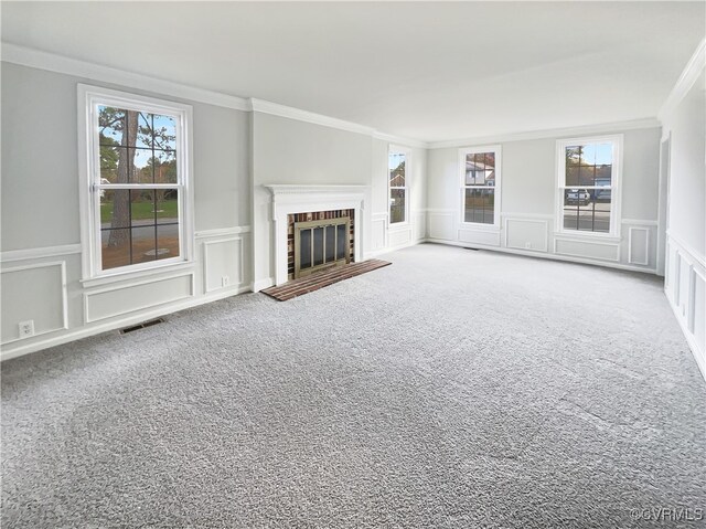 unfurnished living room with a wealth of natural light, crown molding, a fireplace, and carpet floors