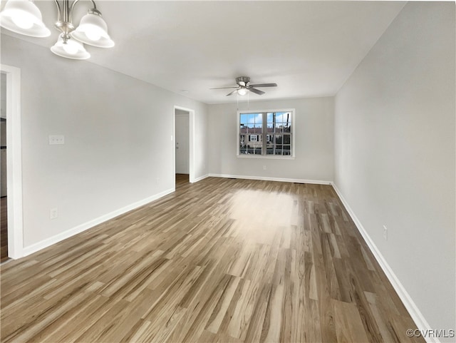 empty room with ceiling fan with notable chandelier and hardwood / wood-style flooring