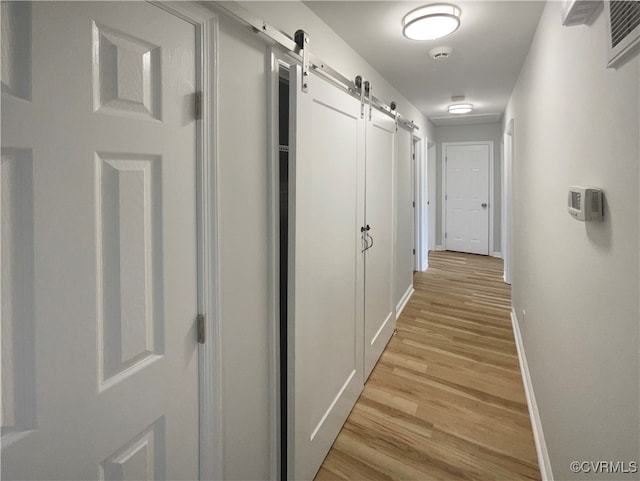 corridor featuring light wood-type flooring and a barn door