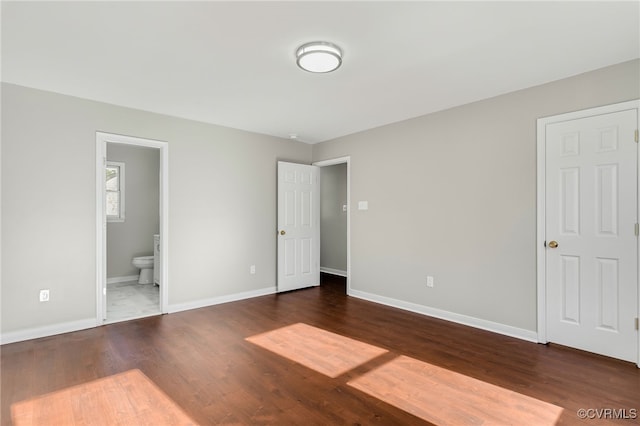 unfurnished bedroom featuring ensuite bath and dark wood-type flooring