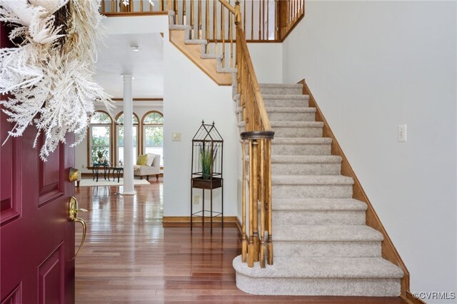 staircase featuring ornate columns, a high ceiling, and hardwood / wood-style flooring