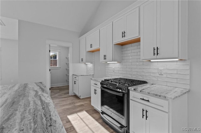 kitchen with lofted ceiling, light wood-style flooring, decorative backsplash, stainless steel gas stove, and white cabinetry