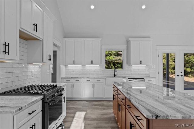 kitchen featuring a sink, white cabinets, brown cabinetry, light stone countertops, and gas range oven