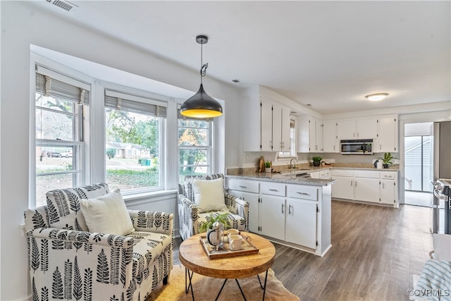 kitchen with sink, dark wood-type flooring, hanging light fixtures, light stone counters, and white cabinets