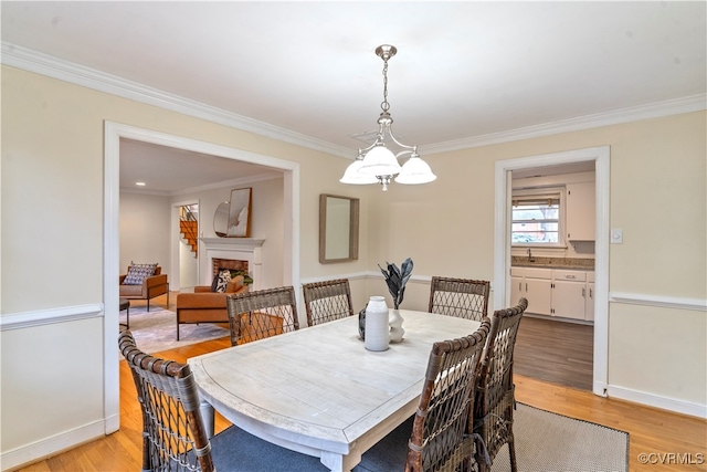 dining area with a notable chandelier, crown molding, light wood-type flooring, and sink