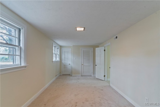 interior space featuring a textured ceiling, light colored carpet, and a healthy amount of sunlight