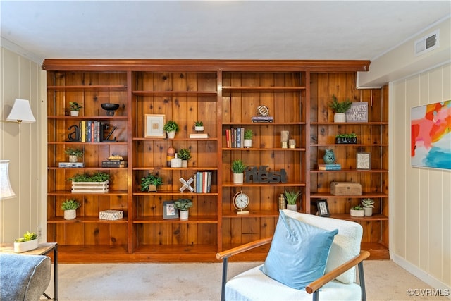 living area with wood walls, crown molding, and light carpet