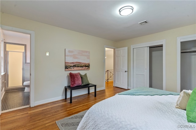 bedroom featuring ensuite bath, multiple closets, and hardwood / wood-style flooring