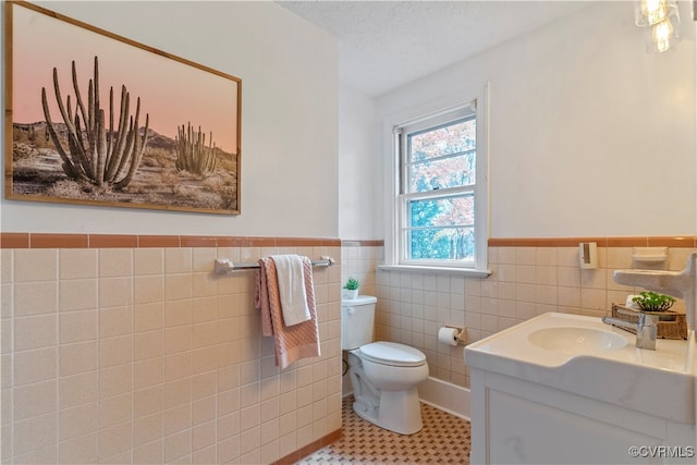 bathroom with tile patterned flooring, a textured ceiling, toilet, vanity, and tile walls