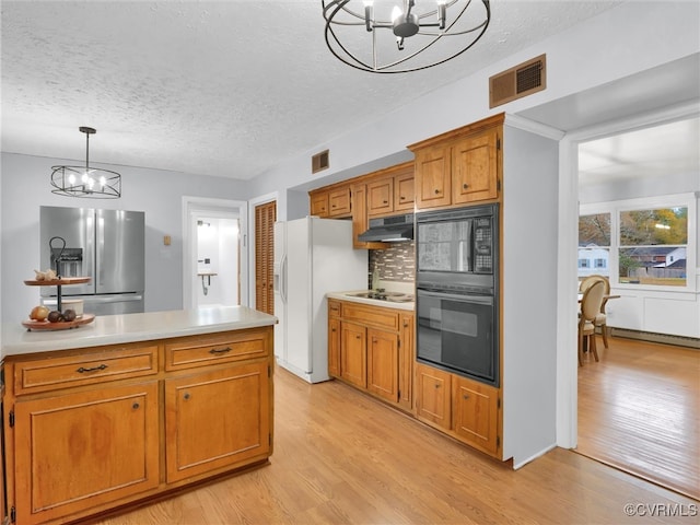 kitchen featuring light wood-type flooring, hanging light fixtures, a notable chandelier, and black appliances