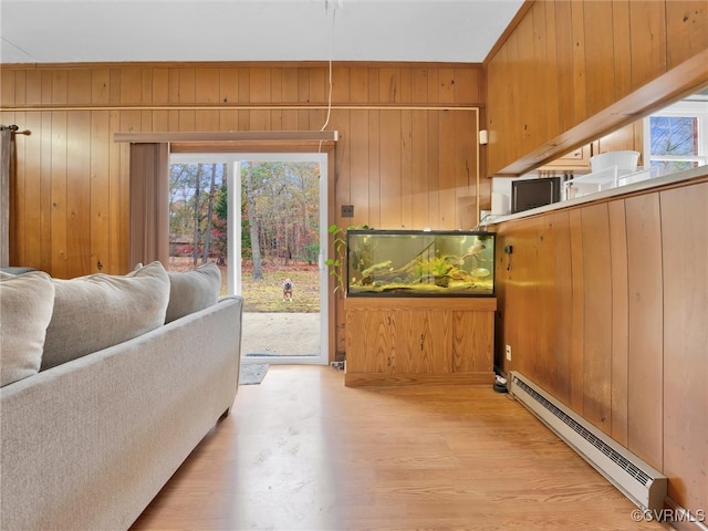 living room with vaulted ceiling, a baseboard radiator, light hardwood / wood-style flooring, and wooden walls