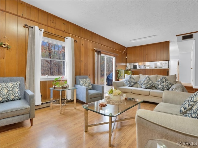 living room featuring a baseboard heating unit, a textured ceiling, wooden walls, and light hardwood / wood-style flooring