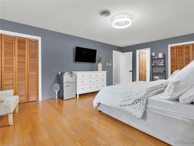 bedroom with light hardwood / wood-style floors and two closets