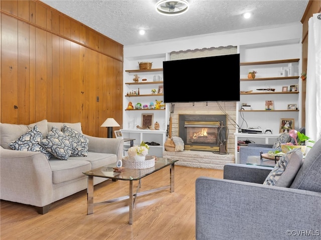 living room with a textured ceiling, wooden walls, light hardwood / wood-style flooring, built in features, and a fireplace