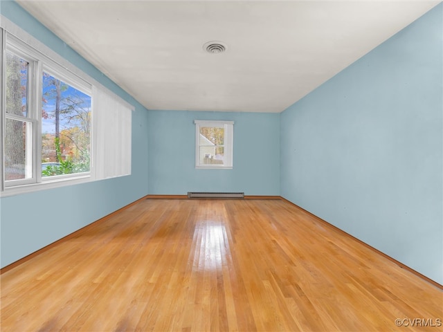 unfurnished room featuring light wood-type flooring, baseboard heating, and a healthy amount of sunlight