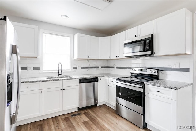 kitchen with stainless steel appliances, white cabinetry, light stone countertops, and sink