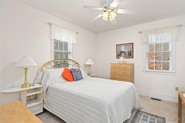 bedroom with multiple windows, ceiling fan, and light carpet