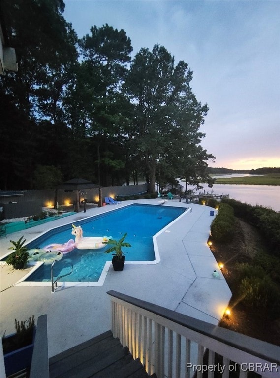 pool at dusk featuring a water view and a hot tub