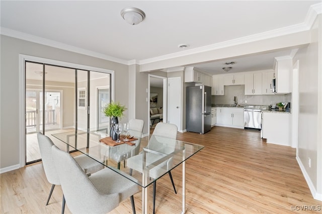 dining room featuring sink, light hardwood / wood-style flooring, and crown molding