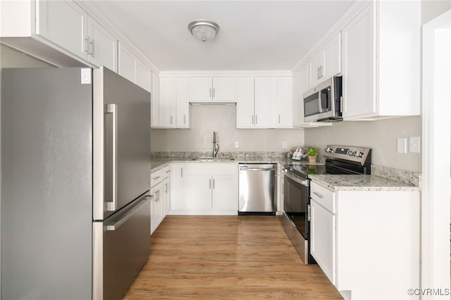 kitchen featuring stainless steel appliances, sink, white cabinetry, light hardwood / wood-style flooring, and light stone countertops