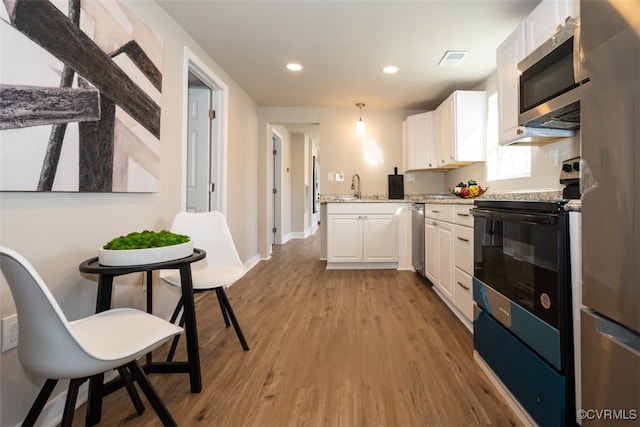 kitchen with appliances with stainless steel finishes, light hardwood / wood-style flooring, white cabinets, and hanging light fixtures