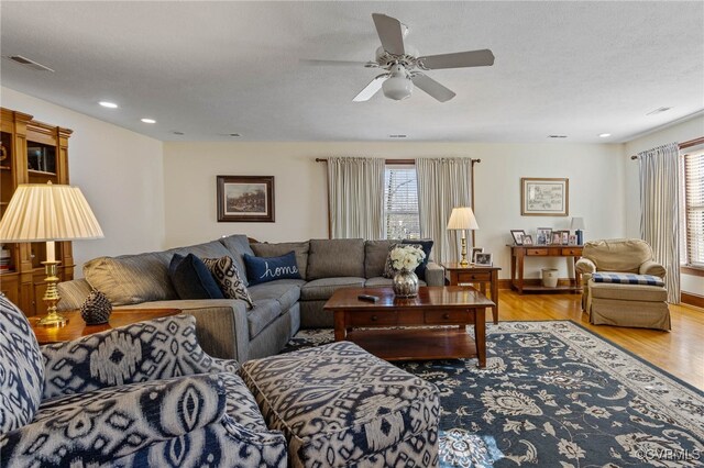 living room featuring a textured ceiling, light wood-type flooring, and ceiling fan