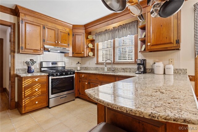 kitchen featuring stainless steel gas stove, light stone counters, sink, and tasteful backsplash