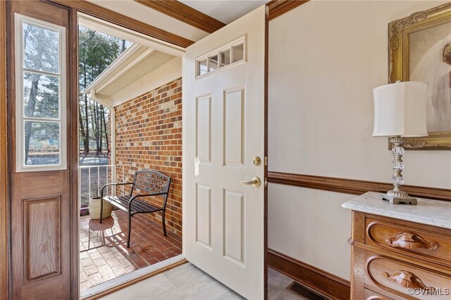 doorway to outside featuring ornamental molding and brick wall