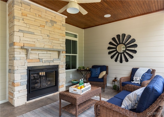 living area with wooden walls, an outdoor stone fireplace, wooden ceiling, concrete flooring, and ceiling fan