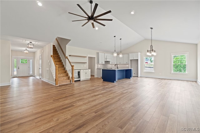 unfurnished living room with high vaulted ceiling, ceiling fan with notable chandelier, and light wood-type flooring