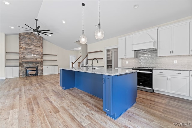 kitchen featuring white cabinets, hanging light fixtures, stainless steel stove, and an island with sink