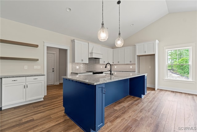 kitchen featuring light stone counters, hardwood / wood-style floors, white cabinets, and an island with sink