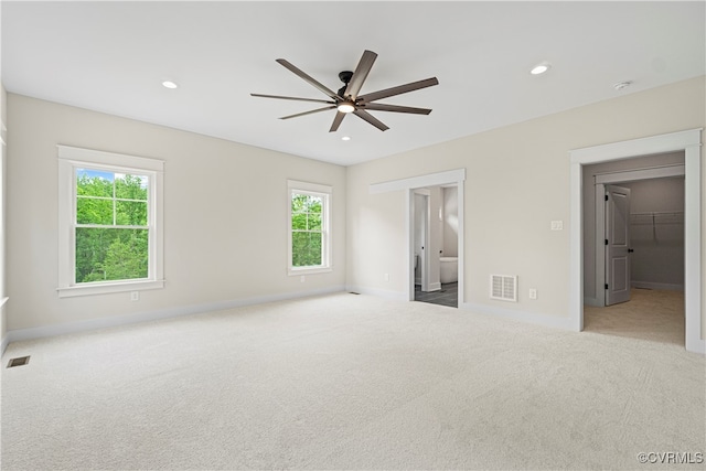 unfurnished bedroom featuring a spacious closet, a closet, ceiling fan, and light carpet