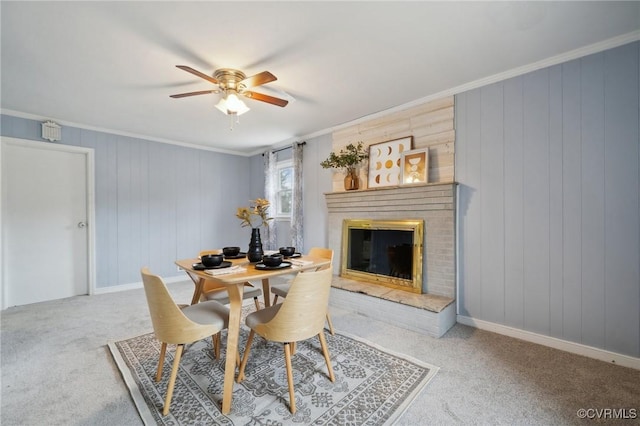 dining area with carpet flooring, ceiling fan, crown molding, wooden walls, and a fireplace