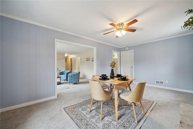 dining room featuring carpet, wood walls, crown molding, and ceiling fan