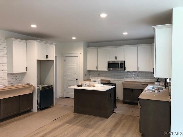 kitchen featuring tasteful backsplash, a kitchen island, sink, white cabinetry, and light wood-type flooring