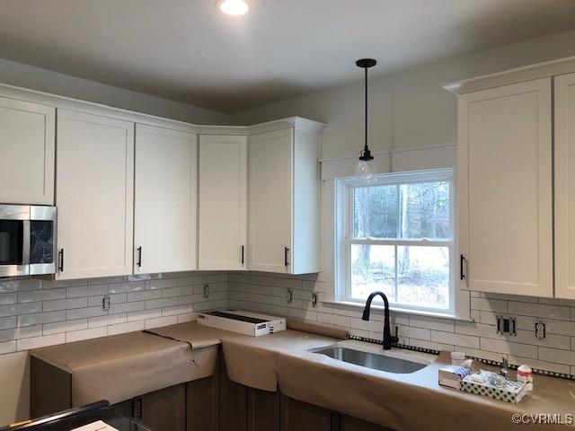 kitchen with decorative light fixtures, sink, decorative backsplash, and white cabinets