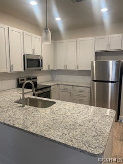 kitchen with white cabinets, light stone countertops, appliances with stainless steel finishes, decorative light fixtures, and kitchen peninsula