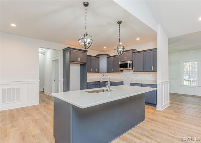 kitchen with sink, backsplash, hanging light fixtures, a center island with sink, and light wood-type flooring